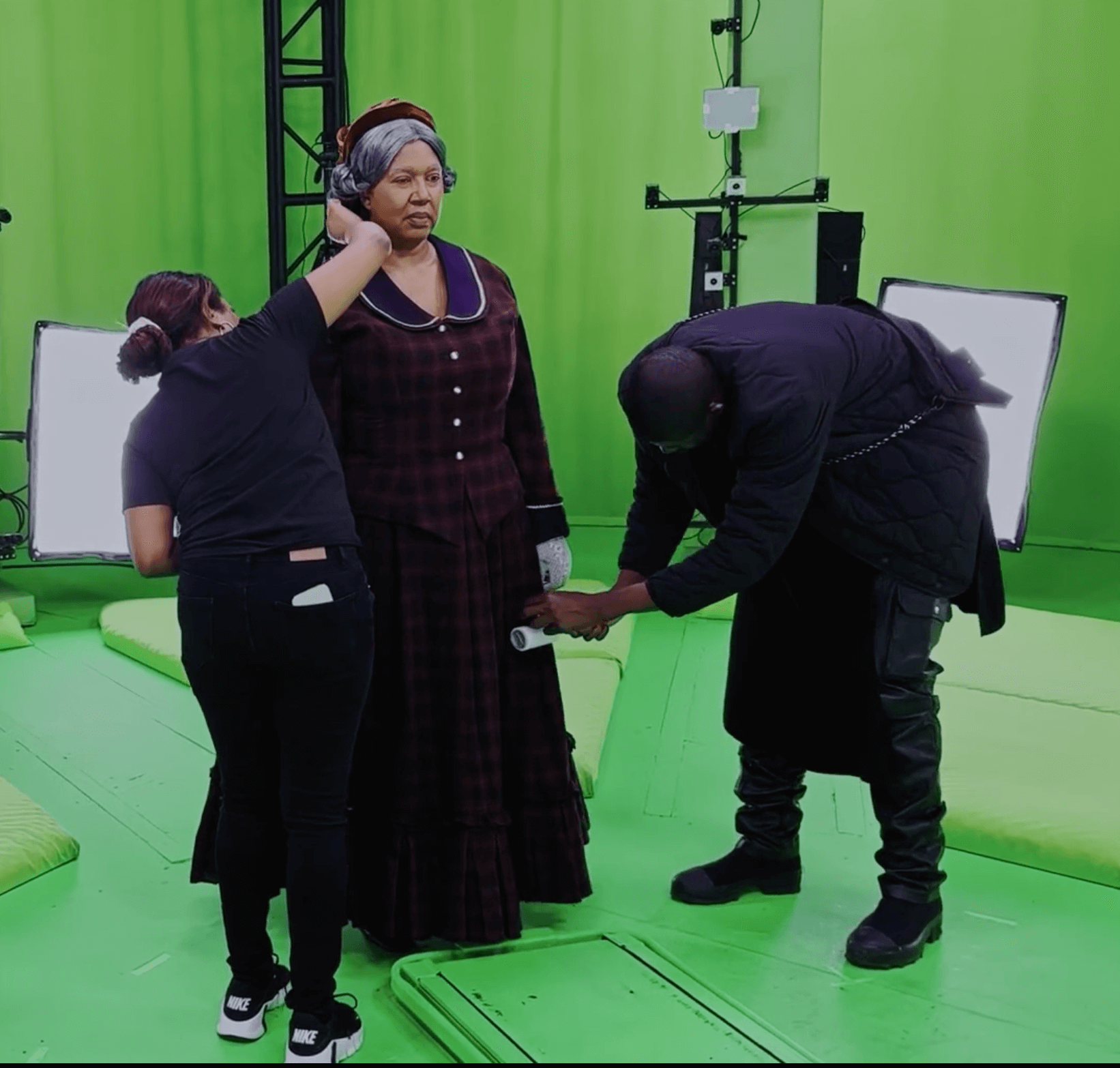 Woman Dressed in old fashioned American clothes while two people help get her ready for a volcap shoot.